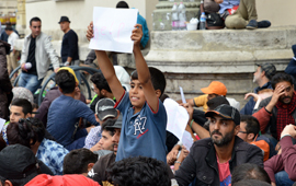 Boy holding up a 'help' sign surrounded by many other refugees