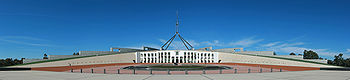 A large white and cream coloured building with grass on its roof. The building is topped with a large flagpole.