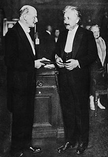 An older Einstein, wearing formal clothes, stands ready to receive an award.