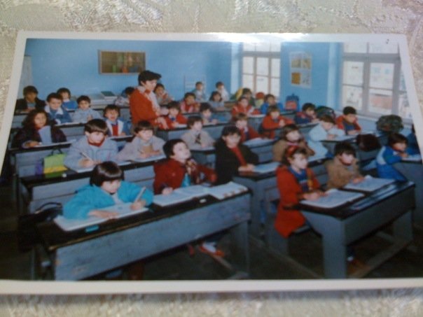 Second grade (first row, left desk, red jacket).