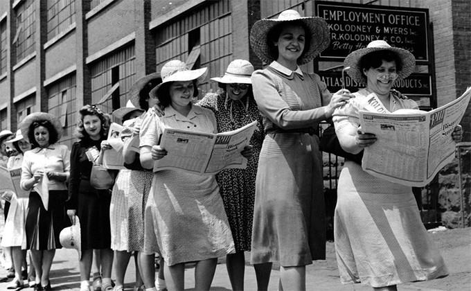 Women standing in a picket line reading the newspaper.