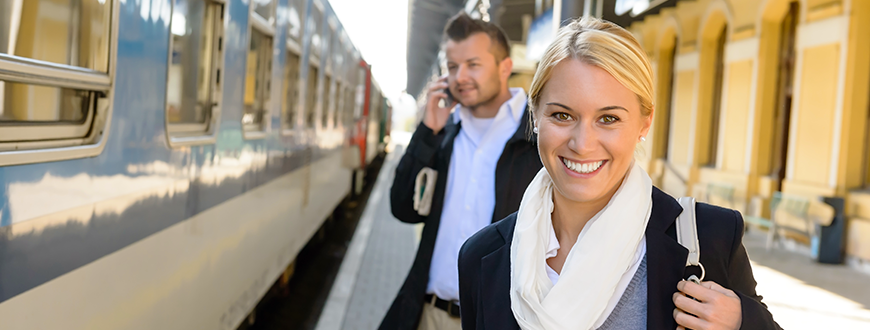 Smiling female, man on phone, business casual dress, waiting to board train at station