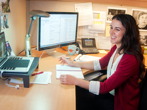 Female staff smiling looking at laptop screen with notebook and pen in hand