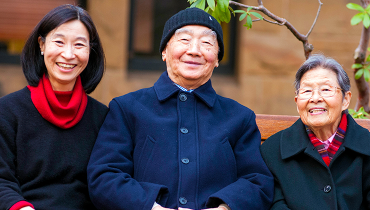 Asian female staff member sitting on a bench next to her elderly father and mother.