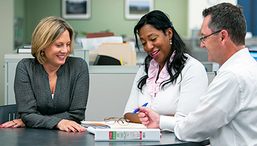 Caucasian female, African American female, and Caucasian male colleagues discussing work project in office