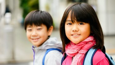 Asian boy and girl wearing backpacks walking to school