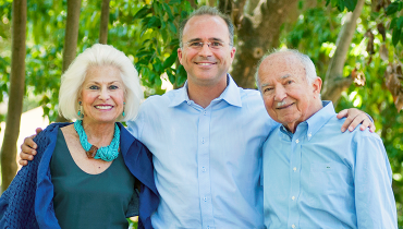 Male staff member with hands on shoulders of his elderly parents.