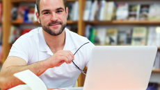 Man studying with laptop and book in library.