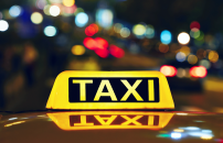 Yellow lit taxi sign on top of taxi, with building lights at night in background.