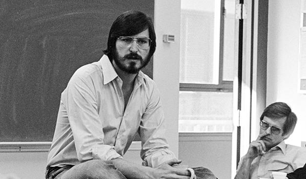 Steve Jobs sitting on a desk teaching students