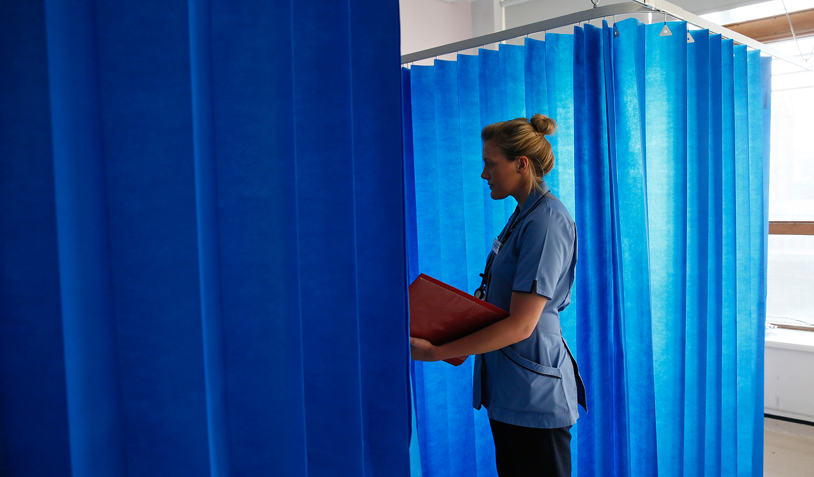 Health care worker talking to a patient behind a privacy curtain | Reuters/Stefan Wermuth
