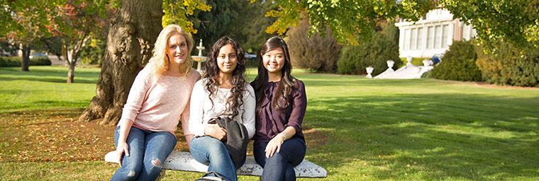 Three female students sitting on bench on green lawn