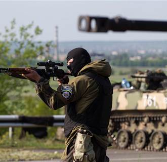 Image: A Ukrainian soldier points his weapon at an approaching car with armoured personnel carriers behind him at a checkpoint near the town of Slaviansk in eastern Ukraine