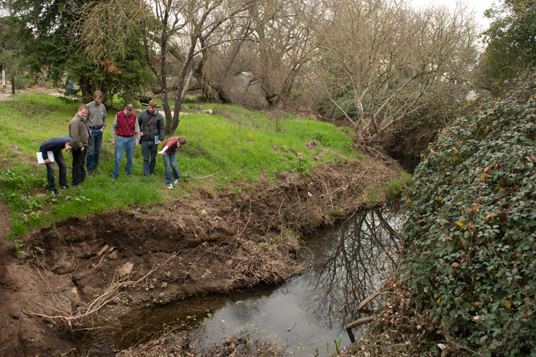 Professor and students on the bank of a small creek.