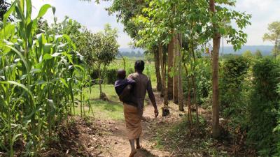 A mother carries her child through crop fields in rural Kenya