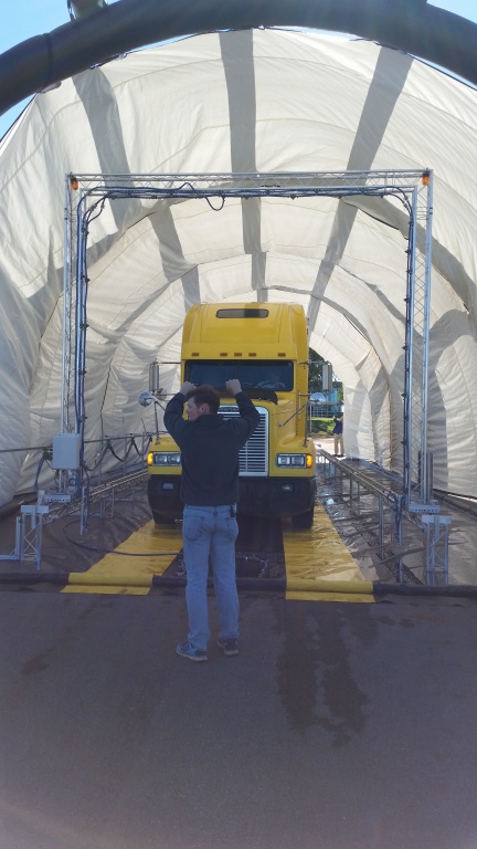 A man uses  hand and arm signals to direct a tractor trailer truck where to park.