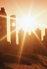 Photograph of sun setting over tall buildings and a freeway.