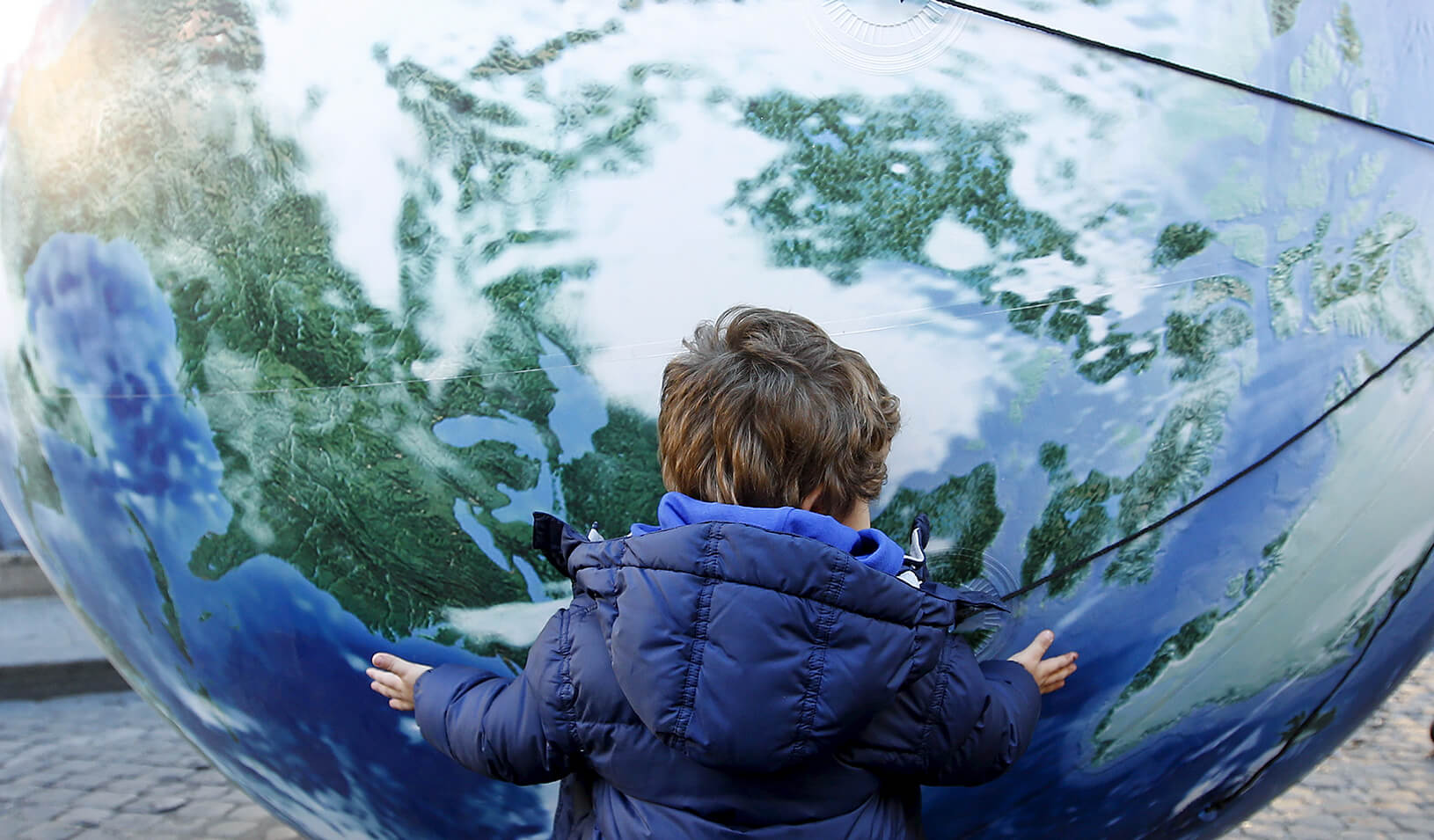 A child embraces a globe shaped balloon | Reuters/Alessandro Bianchi