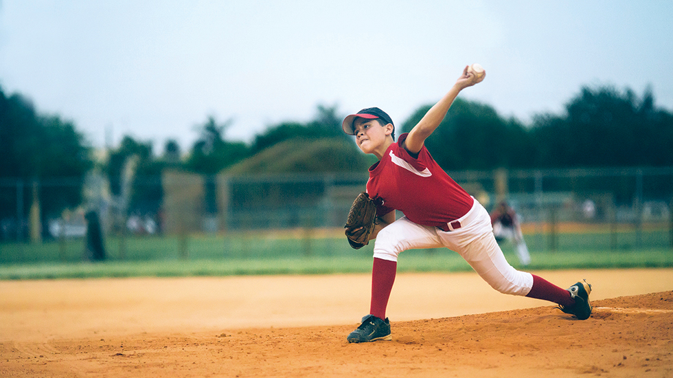 A young boy, on a pitching mound, throwing a baseball