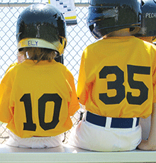 Children in baseball uniforms, sitting on a bench