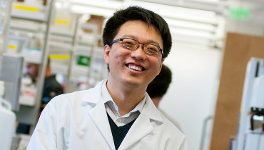 Male Chinese faculty member wearing white lab coat, smiling in laboratory