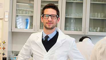 Caucasian male faculty member wearing white lab coat and glasses in lab