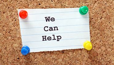 Note on lined paper labelled "We can help" stuck to cork bulletin board with colorful push pins