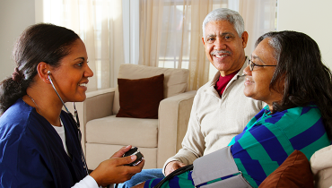 Young African American female nurse wearing stethoscope measuring blood pressure of older African American couple.