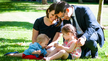 Male faculty member with wife playing with their toddler son and daughter on a sunny lawn