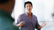 Asian man leading workshop or presentation in front of male and female colleagues.