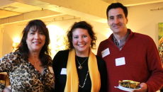 Two female and a male staffer smiling and holding plates of food at a restaurant.