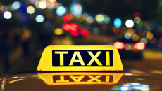 Yellow lit taxi sign on top of taxi, with building lights at night in background.