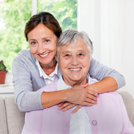 Female caregiver embraces elderly woman