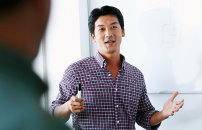 Asian man leading workshop or presentation in front of male and female colleagues.