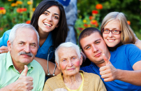 Two seniors, their grandchildren and a nurse, smiling and holding thumbs up.