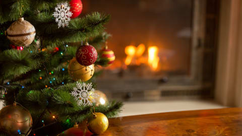 Un sapin de Noël décoré de boules et de guirlandes lumineuses devant un feu de cheminée