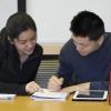 Tutor helping student, looking at notebook together, smiling