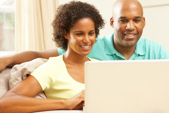 A man and a woman, smiling, using a laptop computer.