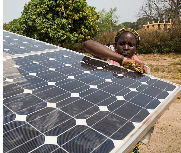 A woman cleans a solar panel that powers the drip irrigation system in a rural village in Benin.