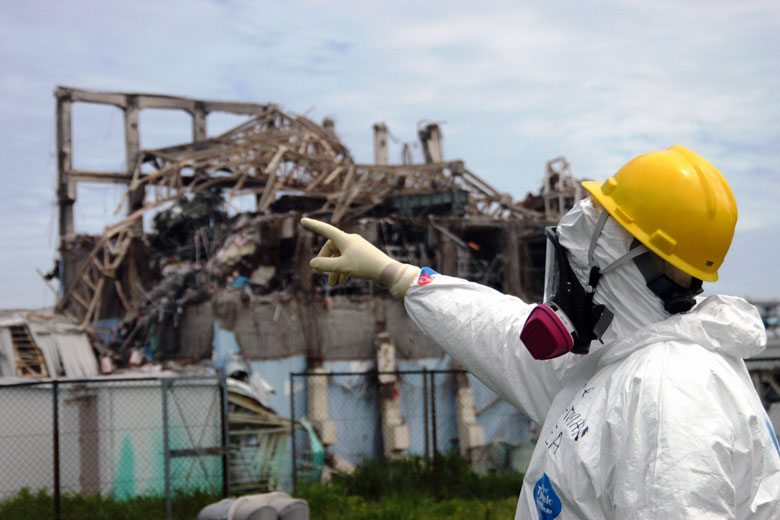man in hazmat suit pointing to damaged Fukushima reactor