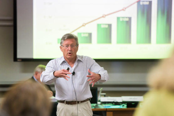 John Etchemendy speaking with a chart on a screen behind him.