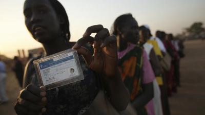 A Southern Sudanese woman displays her voter registration card as she waits in a long line to cast her vote.