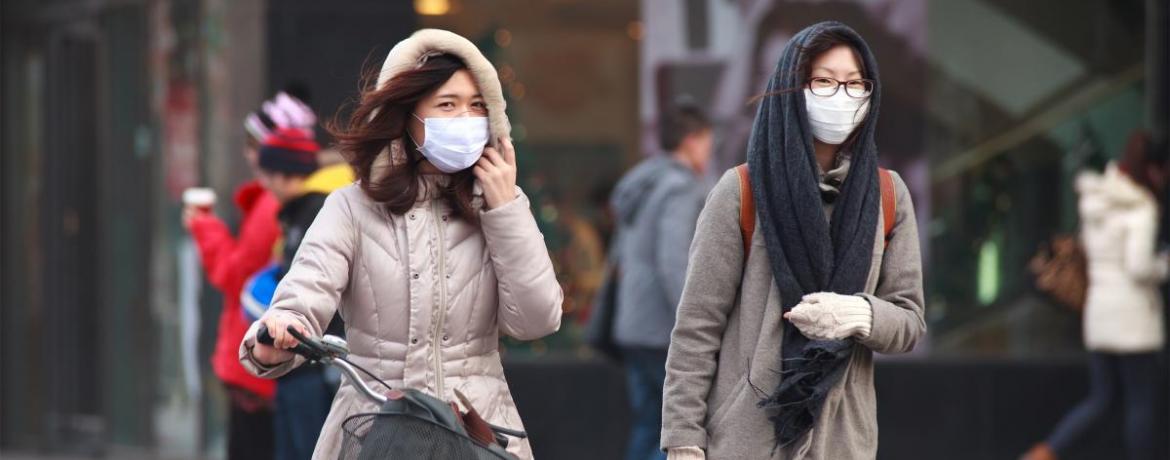 Two young women walk down a Beijing street, each wearing a protective air pollution mask.