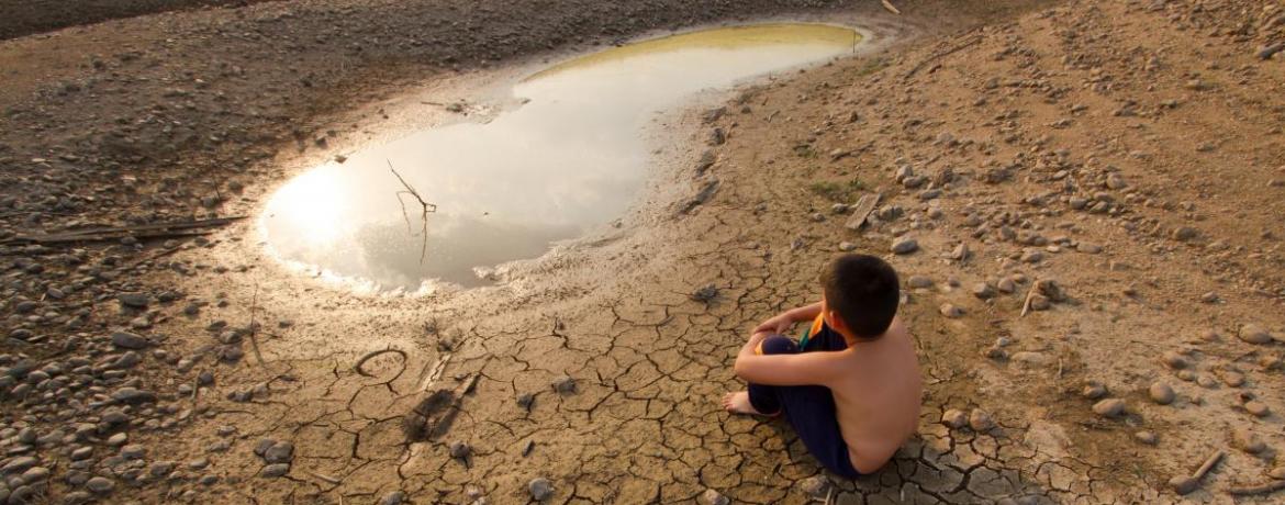 A boy sits on cracked earth near drying lake