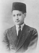 A boy wearing a jacket, a white shirt with a black tie and a fez on his head.