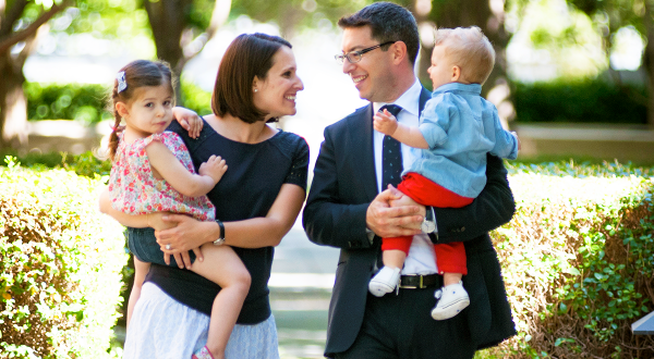 Male faculty member holding toddler son, smiling at wife holding toddler daughter