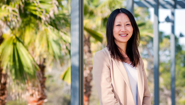 Female Asian faculty member standing on balcony with palm trees in background.
