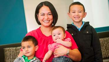 Asian female staff member holding infant daughter and with two young sons.