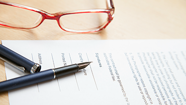 Pair of red-rimmed glasses next to document with pen on desk