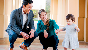 Asian male staff member standing next to Cauasian wife holding their toddler daughter